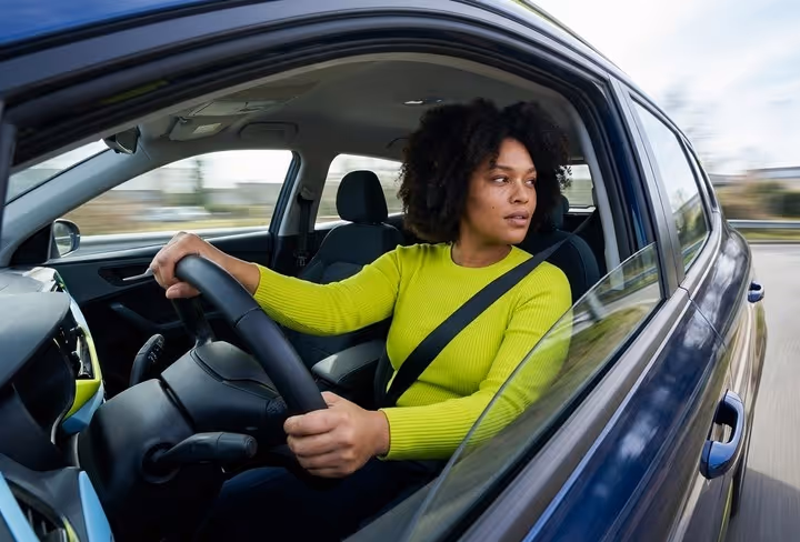 Een vrouw zit in de auto en kijkt over haar schouder op de weg