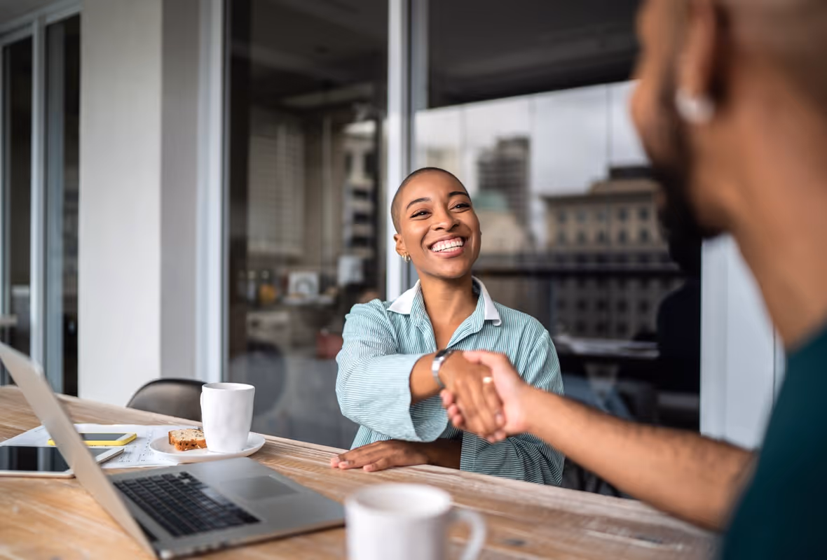 En vrouw schudt lachend de hand van een man.