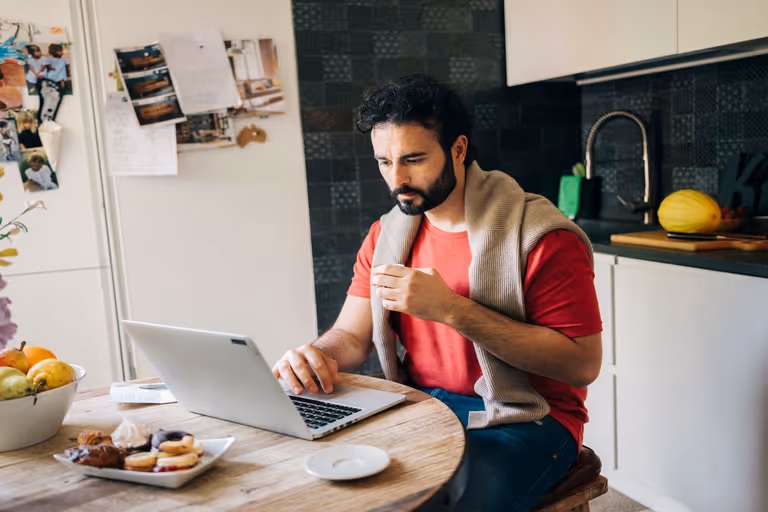 Een man zit achter zijn laptop en kijkt op het scherm.