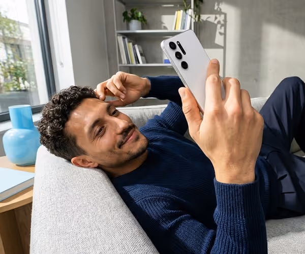 Een man ligt op de bank met zijn telefoon