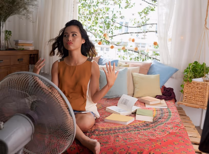 Een vrouw zit puffend van de warmte voor een ventilator