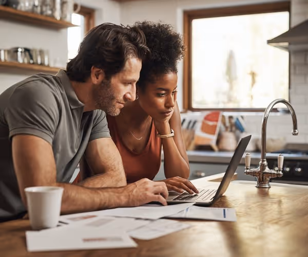 Een stel zit achter de laptop aan de keukentafel met papierwerk